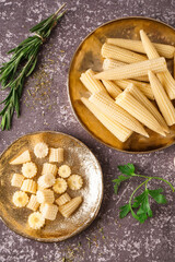 Plates with cut and whole canned baby corn cobs on grey grunge background