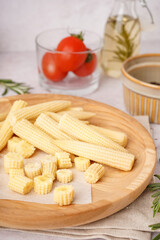 Plate with cut and whole canned baby corn cobs on light background