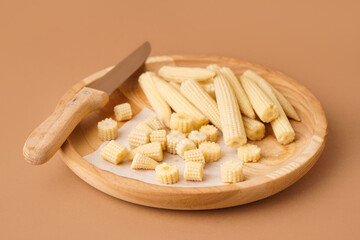 Plate with cut and whole canned baby corn cobs on brown background