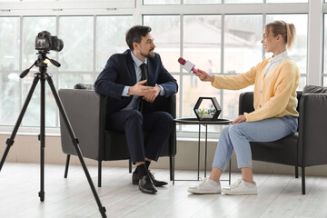 Female journalist with microphone having an interview with man in office