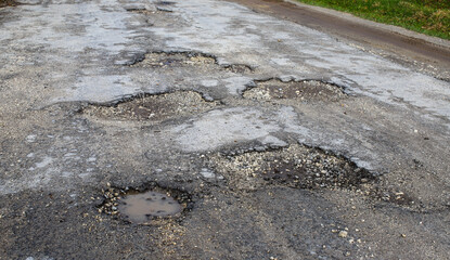 A pothole is a damaged surface of a rural road. Pits and potholes on the road. The dilapidated street needs urgent repair - obrazy, fototapety, plakaty