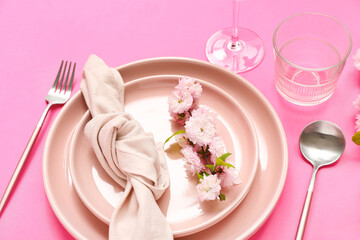 Beautiful table serving with cutlery, blooming tree branch and folded napkin on pink background
