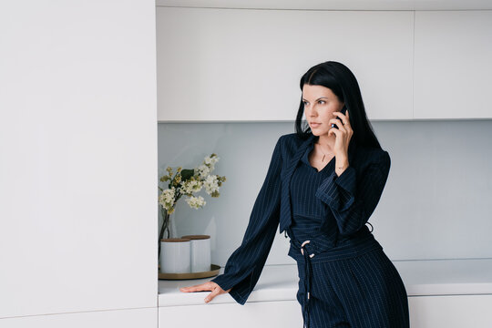 Professional businesswoman in a navy pinstripe suit engaging in a serious conversation on her smartphone with a contemplative expression in a modern office setting