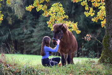 Pferdeliebe. Junge Frau mit langen Haaren streichelt ihr Island Pferd im Herbstwald