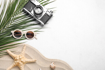 Composition with stylish sunglasses, photo camera, sand, palm leaves and starfish on light background