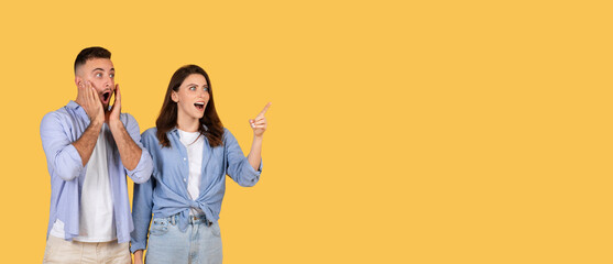 Excited woman pointing away at free space, man shocked, yellow background