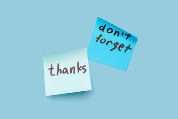 Sticky notes with word THANKS and text DON'T FORGET on blue background