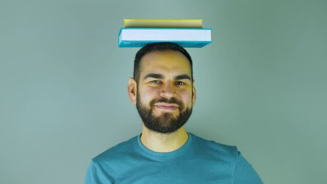 young bearded man with a pile of books on his head pointing his head while looking at camera
