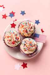 Plate with tasty patriotic cupcakes and flag of USA on pink background. American Independence Day