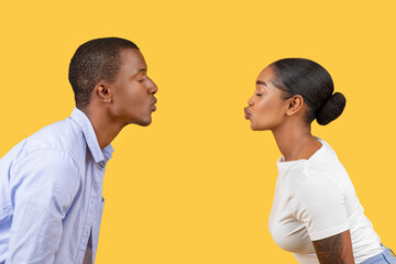 Black couple puckering for a kiss, profiles facing, on yellow background