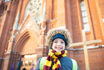 a smiling boy, a child in warm winter clothes, stands near the Catholic Church. A schoolboy goes to...