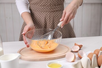Woman whisking eggs in bowl at table indoors, closeup