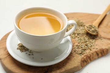 Fennel tea in cup and seeds on white table, closeup