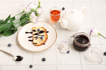 Plate with sweet jam toast, blueberries and glass of tea on white tiled table