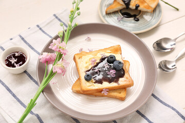 Plates with sweet blueberry jam toasts and flowers on white wooden table