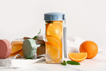 Sports bottles of infused water with orange slices on white table