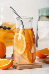 Bottles of infused water with orange slices on white table