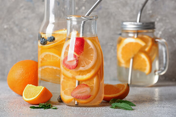 Bottles and mason jar of infused water with orange slices on grey table