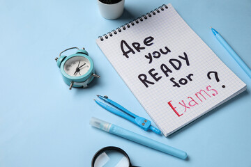 Notebook with question ARE YOU READY FOR EXAMS?, magnifier and alarm clock on blue background
