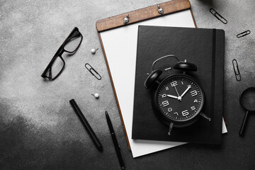Notebooks with alarm clock, eyeglasses and magnifier on dark grunge background