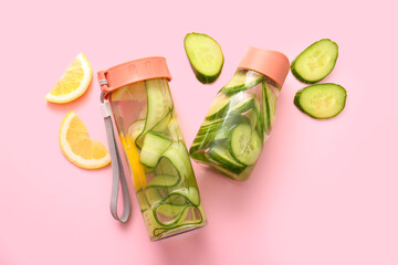 Sports bottles of infused water with cucumber slices on pink background