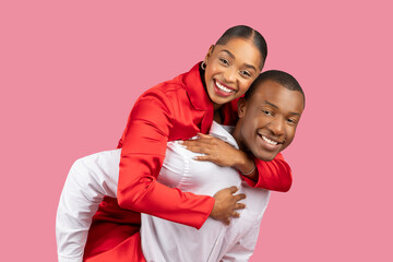 Obraz premium Joyful black couple with woman piggybacking on man against pink backdrop