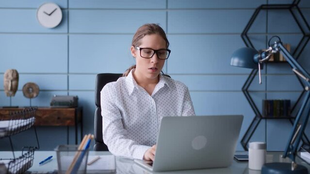 young woman in white shirt and eyeglasses sit at table desk in office, working at laptop. frustrated and worried, frowns, gives up and closes computer to have a break and breath out.