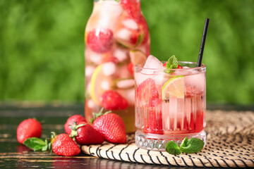 Glass and bottle of strawberry lemonade on wooden table outdoors