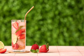 Glass of strawberry lemonade on pink tile table outdoors