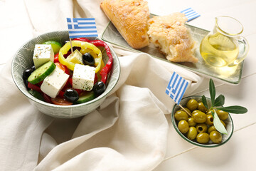 Dishes with ciabatta bread, salad, green olives and flags of Greece on white wooden table