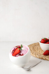 Bowl of strawberry ice cream and spoon on white table, closeup