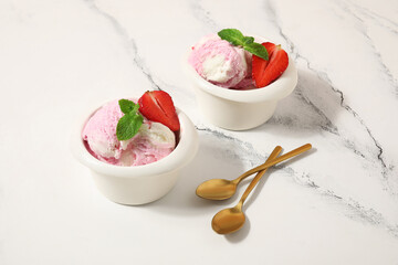Bowls of strawberry ice cream and spoons on grunge background