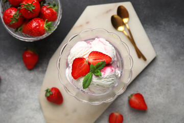 Bowl of vanilla ice cream with strawberries, mint and golden spoons on grey grunge table
