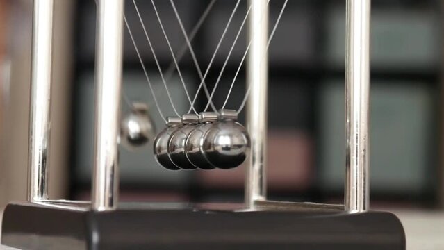 Close-up of Newton's cradle on the table and a child's fingers pulling back one ball and releasing it starting the pendulum