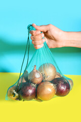 Female hand with different kinds of onion in eco bag on color background