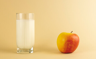 A glass of milk and an apple on a beige background. The concept of diet and weight loss.