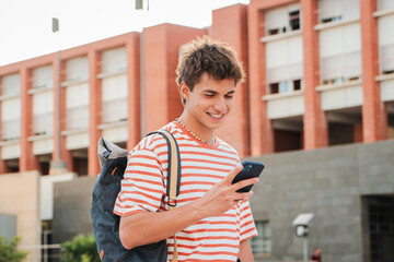 Male student having fun with a cellphone posting on the social media at university campus. Real...