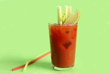 Glass of bloody mary with celery and lime on green background