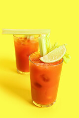 Glasses of bloody mary with celery and lime on yellow background