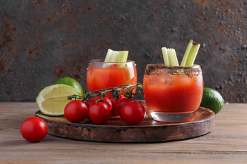 Board with glasses of bloody mary and celery on wooden table