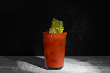 Glass of bloody mary with celery on wooden table against dark green background