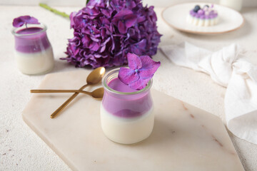 Glasses of panna cotta with beautiful hydrangea flowers on white table