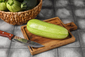 Wooden board with fresh zucchini on black tile background