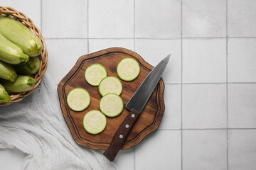Wooden board with fresh cut zucchini on white tile background