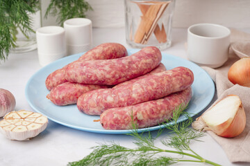 Plate with raw homemade sausages on light background