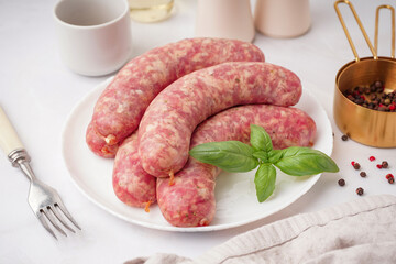 Plate with raw homemade sausages on light background