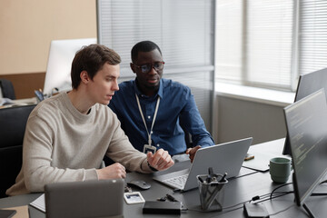 Caucasian male junior IT specialist sitting at table and explaining new cybersecurity software code...