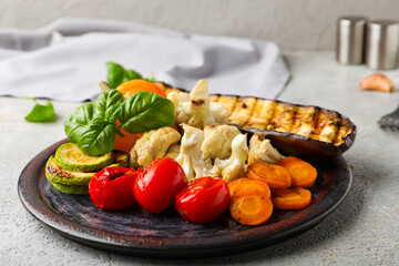 Plate with grilled vegetables and basil on grey background