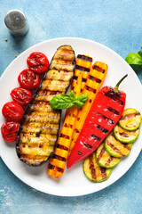 Plate with grilled vegetables and basil on blue background