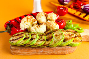 Board with grilled vegetables on orange background